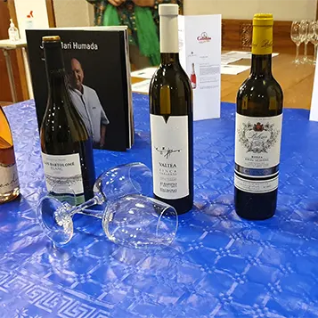 Demostraciones de varias botellas de vino encima de una mesa con un mantel azul y junto a dos copas de vino.