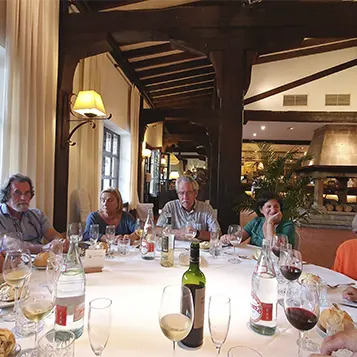 Mesa redonda de un comedor de un restaurante rodeado de personas que están disfrutando de una comida y de diferentes tipos de vino.